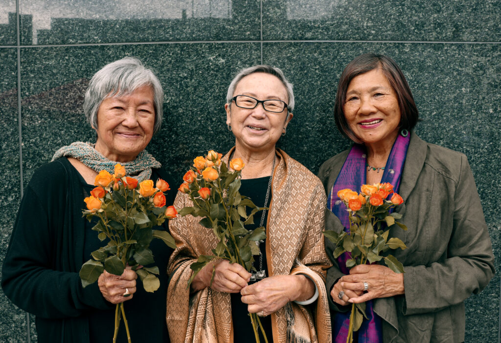 The Last Hoisan Poets, Photo by Megan Wong: The Last Hoisan Poets, Nellie Wong, Flo Oy Wong and Genny Lim, with smiles as warm as the vibrant golden yellow and orange roses bouquets that they hold in their hands, stand in front of the shiny speckled gray granite wall in San Francisco’s Union Square.